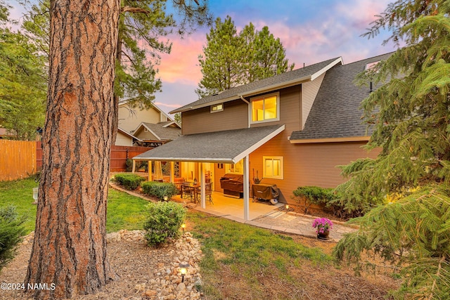 back house at dusk with a patio area and a lawn