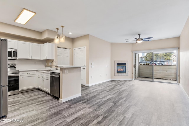 kitchen with white cabinetry, hanging light fixtures, appliances with stainless steel finishes, kitchen peninsula, and a tile fireplace