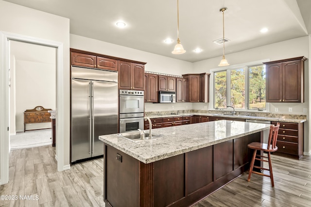 kitchen with sink, a kitchen island with sink, decorative light fixtures, and stainless steel appliances