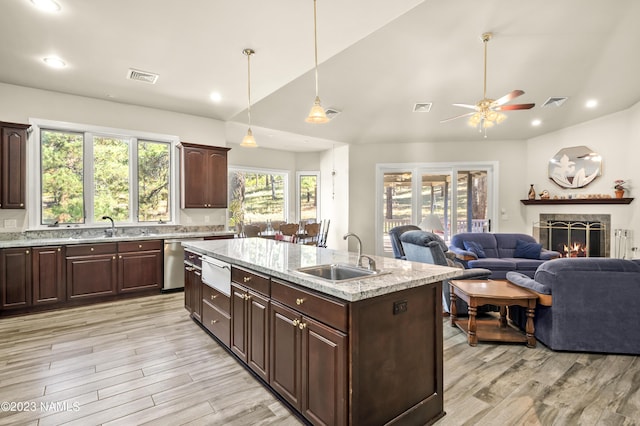 kitchen featuring decorative light fixtures, light hardwood / wood-style floors, sink, stainless steel dishwasher, and a center island with sink