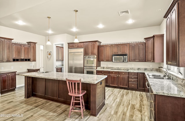 kitchen featuring hanging light fixtures, sink, a kitchen island, light wood-type flooring, and stainless steel appliances