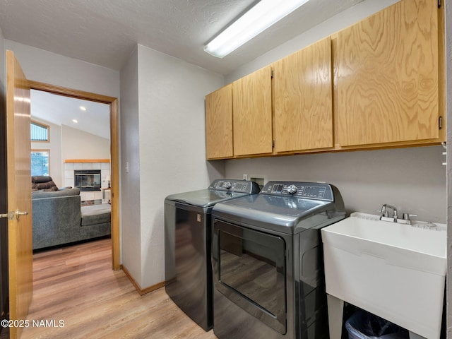 laundry room featuring washing machine and clothes dryer, a tiled fireplace, light wood-style floors, cabinet space, and a sink