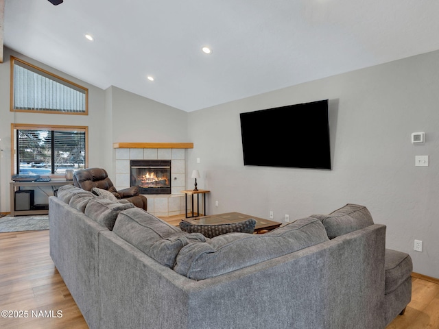 living area with recessed lighting, a tiled fireplace, vaulted ceiling, and light wood finished floors