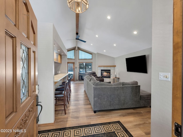 living room featuring ceiling fan, a tiled fireplace, beamed ceiling, light wood-style flooring, and recessed lighting