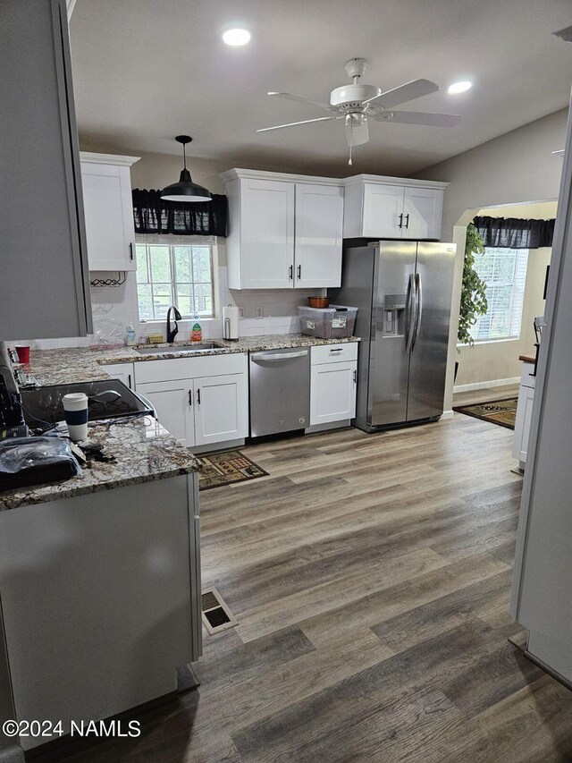 kitchen featuring hardwood / wood-style floors, appliances with stainless steel finishes, white cabinets, sink, and light stone counters