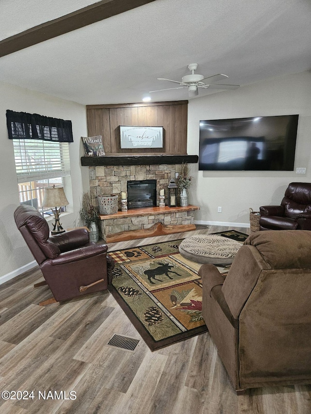 living room featuring wood-type flooring, a stone fireplace, a textured ceiling, and ceiling fan