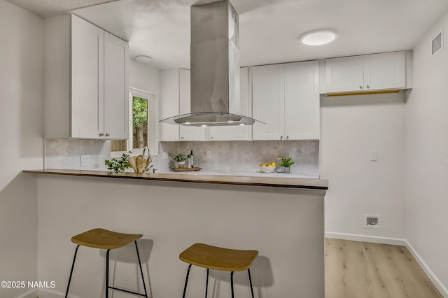 4972 E Snow Shoe Way, Flagstaff, AZ 86004 - kitchen featuring island exhaust hood, light wood finished floors, a breakfast bar, and white cabinets