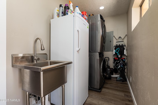 clothes washing area with sink, dark wood-type flooring, a textured ceiling, and stacked washer / drying machine