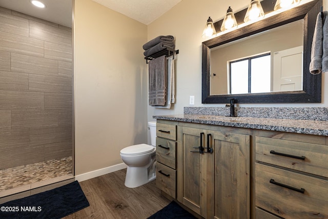 bathroom with toilet, wood-type flooring, vanity, and a tile shower