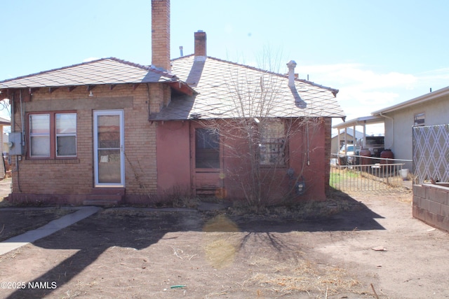 back of property with brick siding, a chimney, and fence