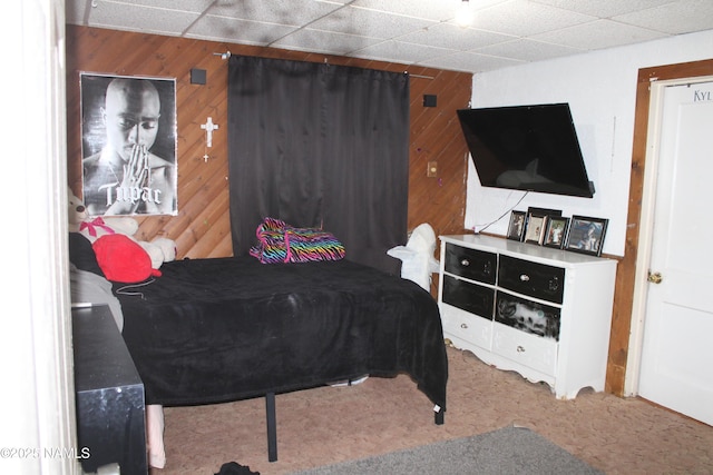 carpeted bedroom featuring a paneled ceiling and wooden walls