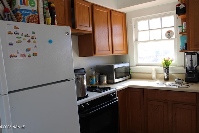 kitchen with range with gas stovetop, freestanding refrigerator, light countertops, stainless steel microwave, and brown cabinets