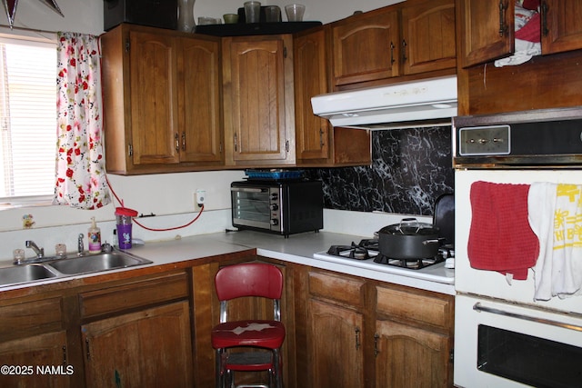 kitchen with white appliances, a sink, light countertops, exhaust hood, and brown cabinets