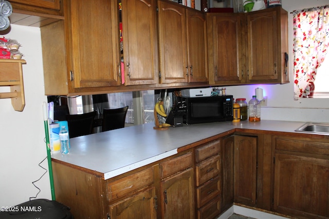 kitchen featuring light countertops, brown cabinetry, black microwave, and a sink