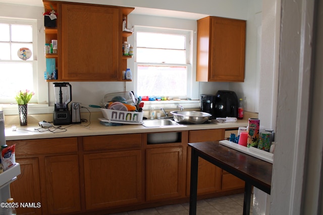 kitchen with open shelves, brown cabinetry, light countertops, and a sink