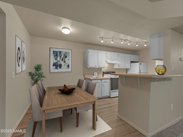 kitchen featuring light wood-type flooring, under cabinet range hood, white appliances, light countertops, and baseboards