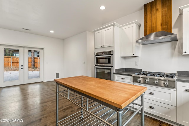 kitchen with appliances with stainless steel finishes, white cabinetry, french doors, dark wood-type flooring, and wall chimney exhaust hood