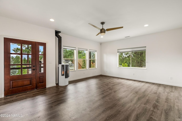 unfurnished living room featuring ceiling fan, a wood stove, and dark hardwood / wood-style flooring