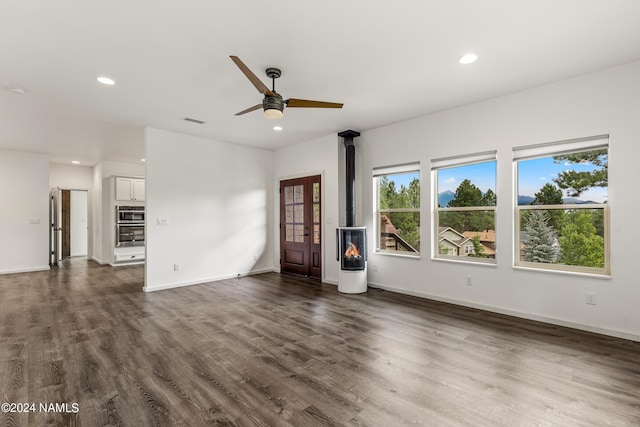 unfurnished living room featuring a wood stove, ceiling fan, and dark wood-type flooring