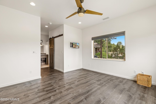 spare room featuring ceiling fan, a barn door, and dark hardwood / wood-style flooring