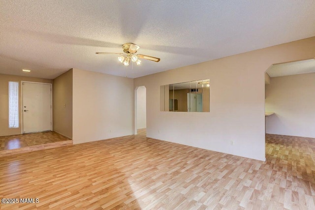 empty room with arched walkways, a textured ceiling, wood finished floors, and a ceiling fan