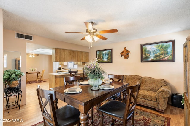 dining room with a textured ceiling, light wood-style floors, visible vents, and ceiling fan