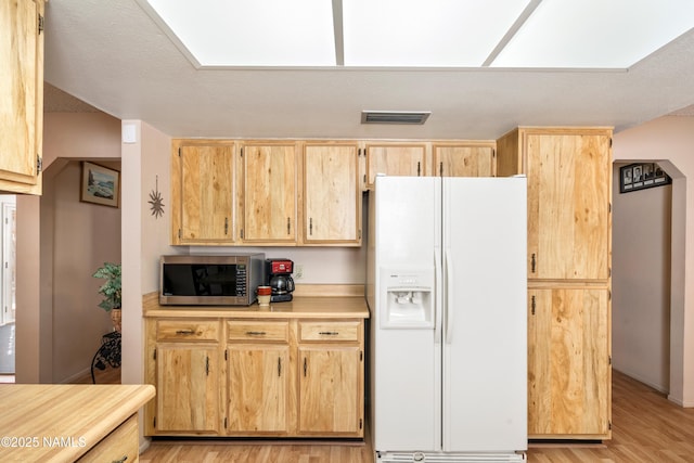 kitchen featuring visible vents, light wood-style flooring, light brown cabinetry, white refrigerator with ice dispenser, and stainless steel microwave