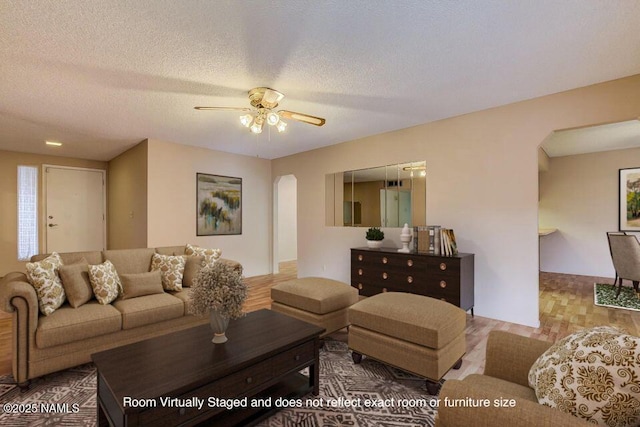 living room with wood finished floors, a ceiling fan, arched walkways, and a textured ceiling