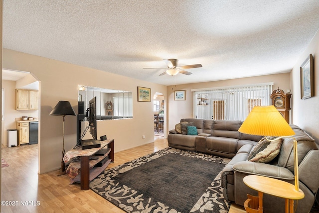 living area featuring light wood finished floors, arched walkways, a textured ceiling, and ceiling fan