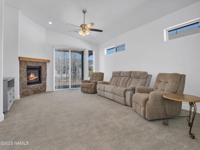 carpeted living room with ceiling fan, vaulted ceiling, and a stone fireplace