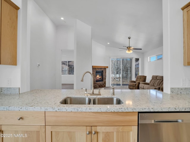 kitchen featuring a fireplace, sink, stainless steel dishwasher, light stone counters, and light brown cabinetry