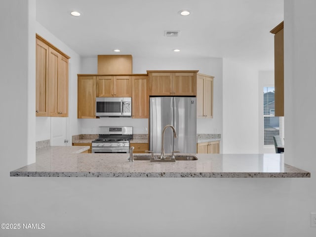 kitchen with appliances with stainless steel finishes, sink, light stone counters, and kitchen peninsula