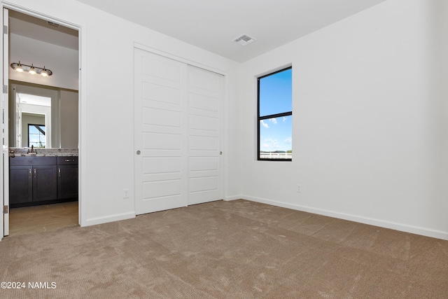 unfurnished bedroom featuring light colored carpet, connected bathroom, a closet, and multiple windows