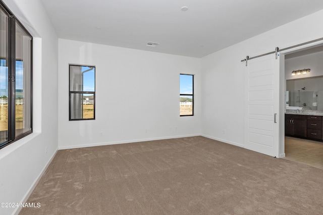 unfurnished bedroom featuring light carpet, sink, ensuite bath, and a barn door