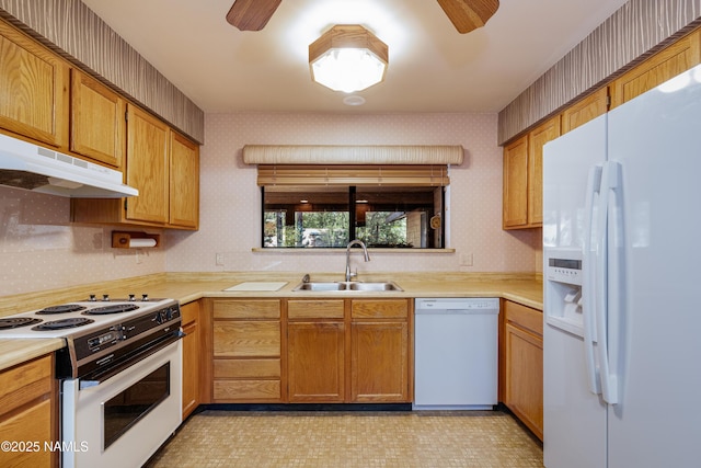 kitchen featuring a sink, wallpapered walls, under cabinet range hood, and white appliances