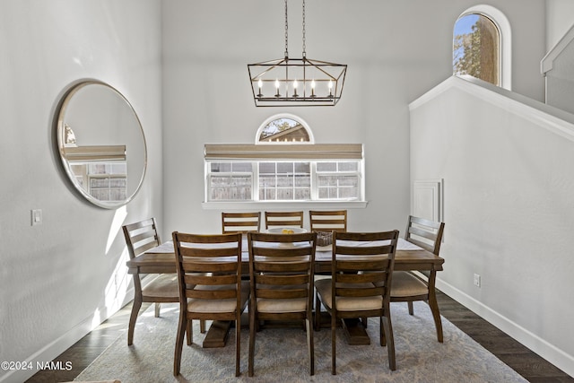 dining area featuring dark wood-type flooring, a towering ceiling, and an inviting chandelier