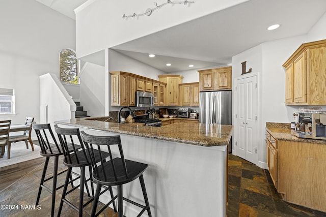 kitchen with a kitchen breakfast bar, kitchen peninsula, stainless steel appliances, and dark stone countertops