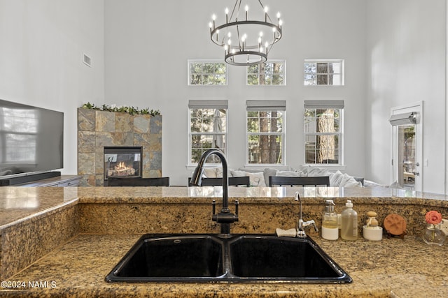 kitchen with a notable chandelier, a towering ceiling, hanging light fixtures, a tile fireplace, and sink