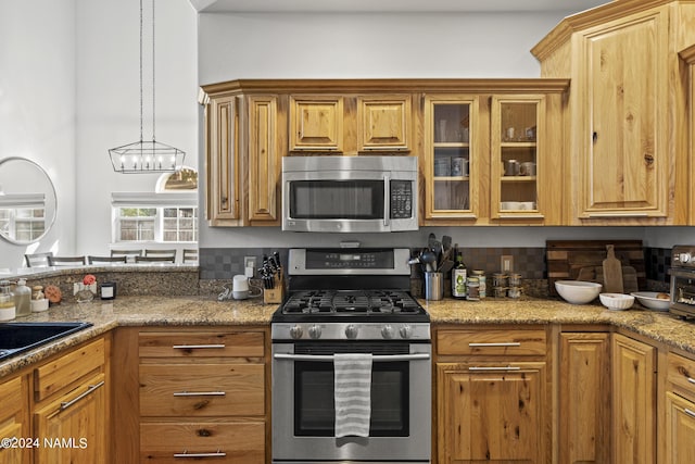 kitchen with decorative light fixtures, light stone countertops, stainless steel appliances, and tasteful backsplash