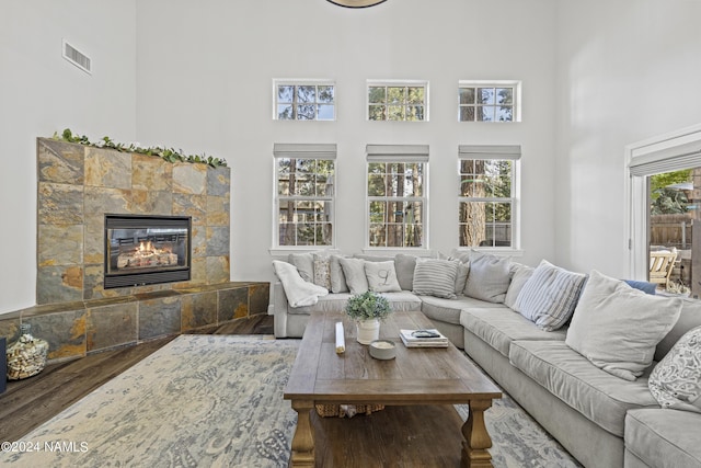 living room featuring a towering ceiling, wood-type flooring, and a tiled fireplace