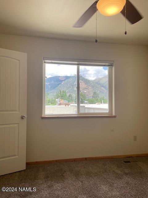 carpeted spare room featuring a mountain view and ceiling fan