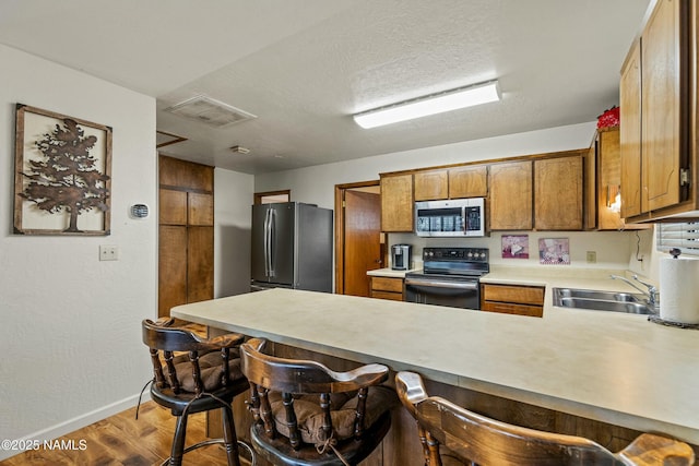 kitchen featuring visible vents, brown cabinets, appliances with stainless steel finishes, a peninsula, and a sink