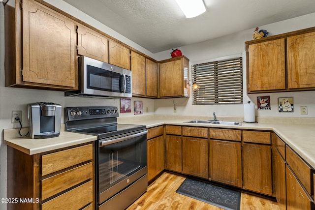 kitchen featuring light wood-type flooring, brown cabinets, a sink, appliances with stainless steel finishes, and light countertops