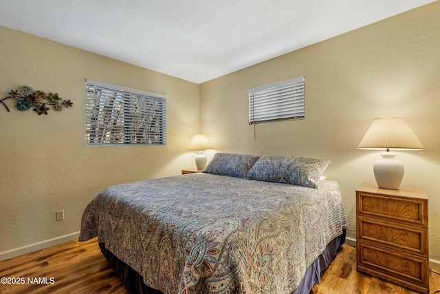 bedroom featuring baseboards, wood finished floors, and a textured wall