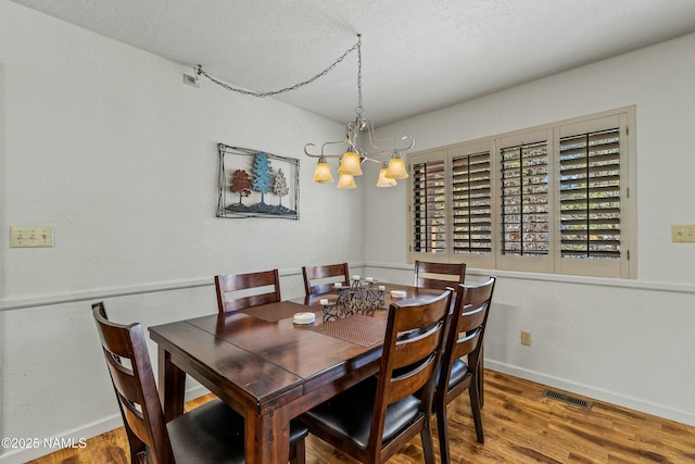 dining room featuring visible vents, a notable chandelier, a textured ceiling, wood finished floors, and baseboards