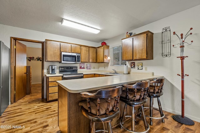 kitchen with light countertops, a peninsula, light wood-type flooring, and appliances with stainless steel finishes