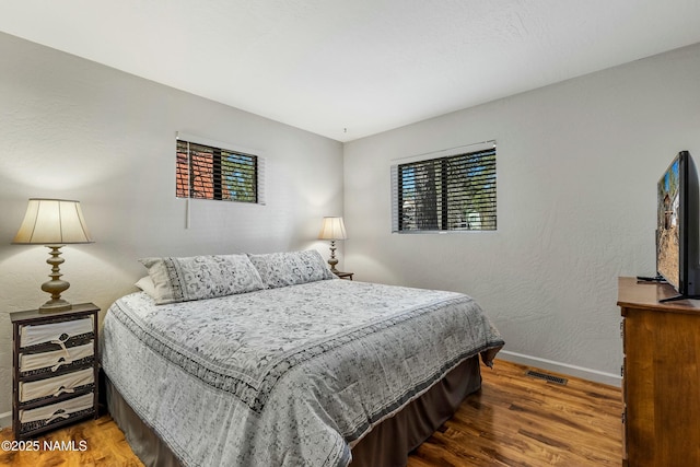 bedroom with a textured wall, visible vents, baseboards, and wood finished floors