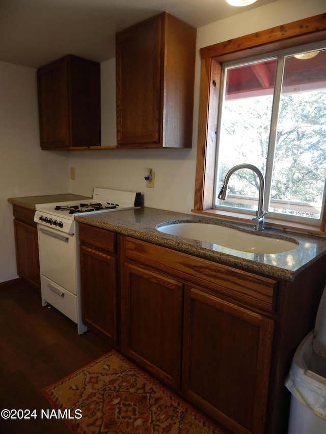 kitchen with sink, dark stone counters, dark hardwood / wood-style floors, and white range with gas cooktop