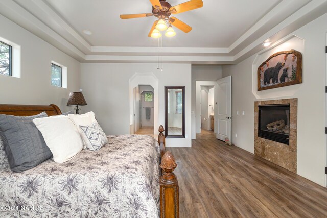 bedroom with ceiling fan, hardwood / wood-style floors, a tray ceiling, and a fireplace