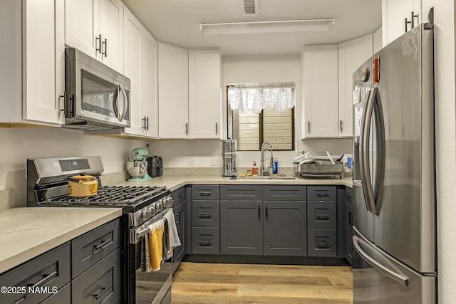 kitchen featuring gray cabinetry, light stone counters, stainless steel appliances, light hardwood / wood-style floors, and white cabinets